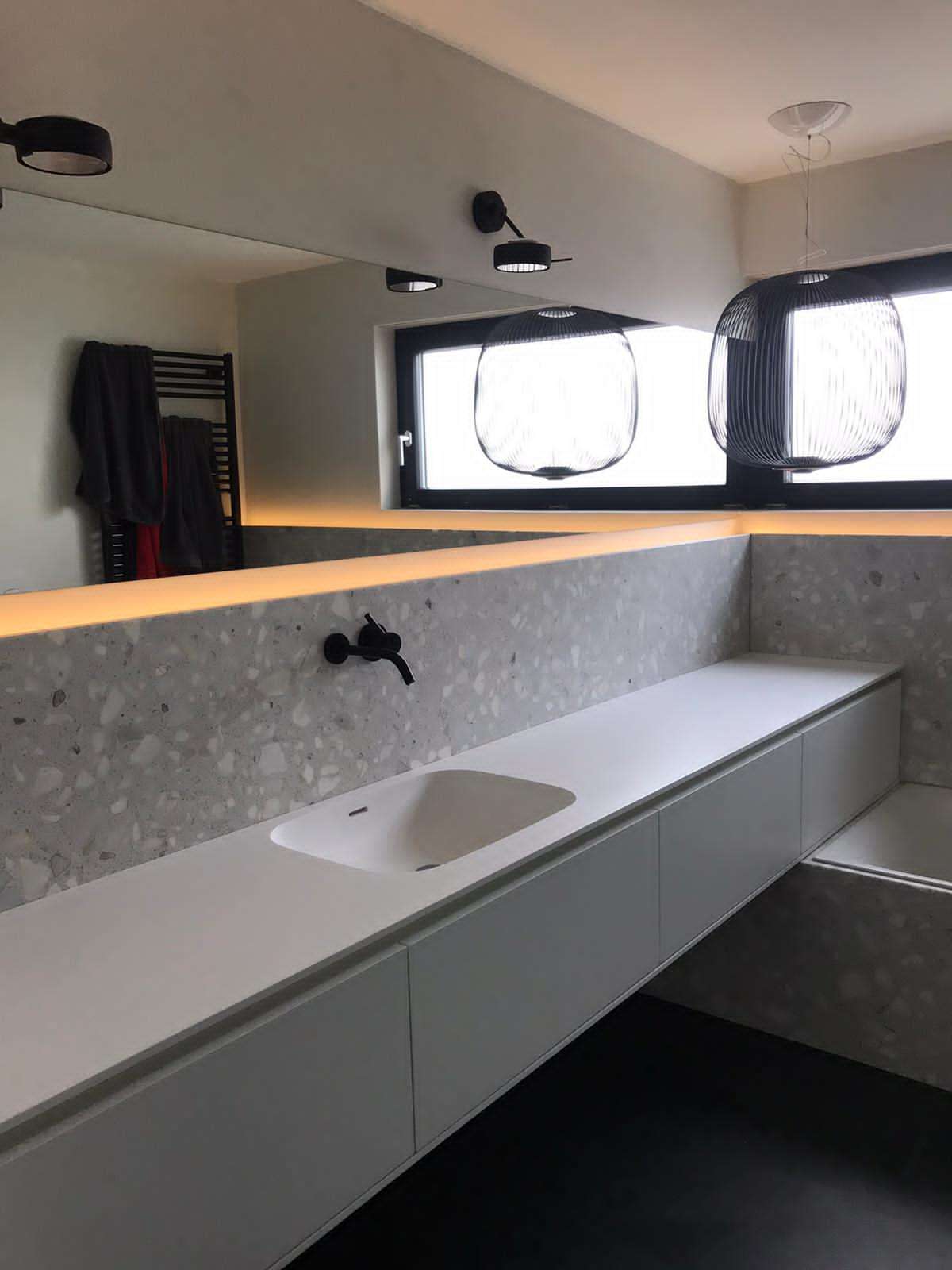 Freihängendes Badezimmermöbel mit fugenlosem Corian Waschtisch. Spiegelband über die Breite des Raums. Wasserhahn aus der Wand kommend.