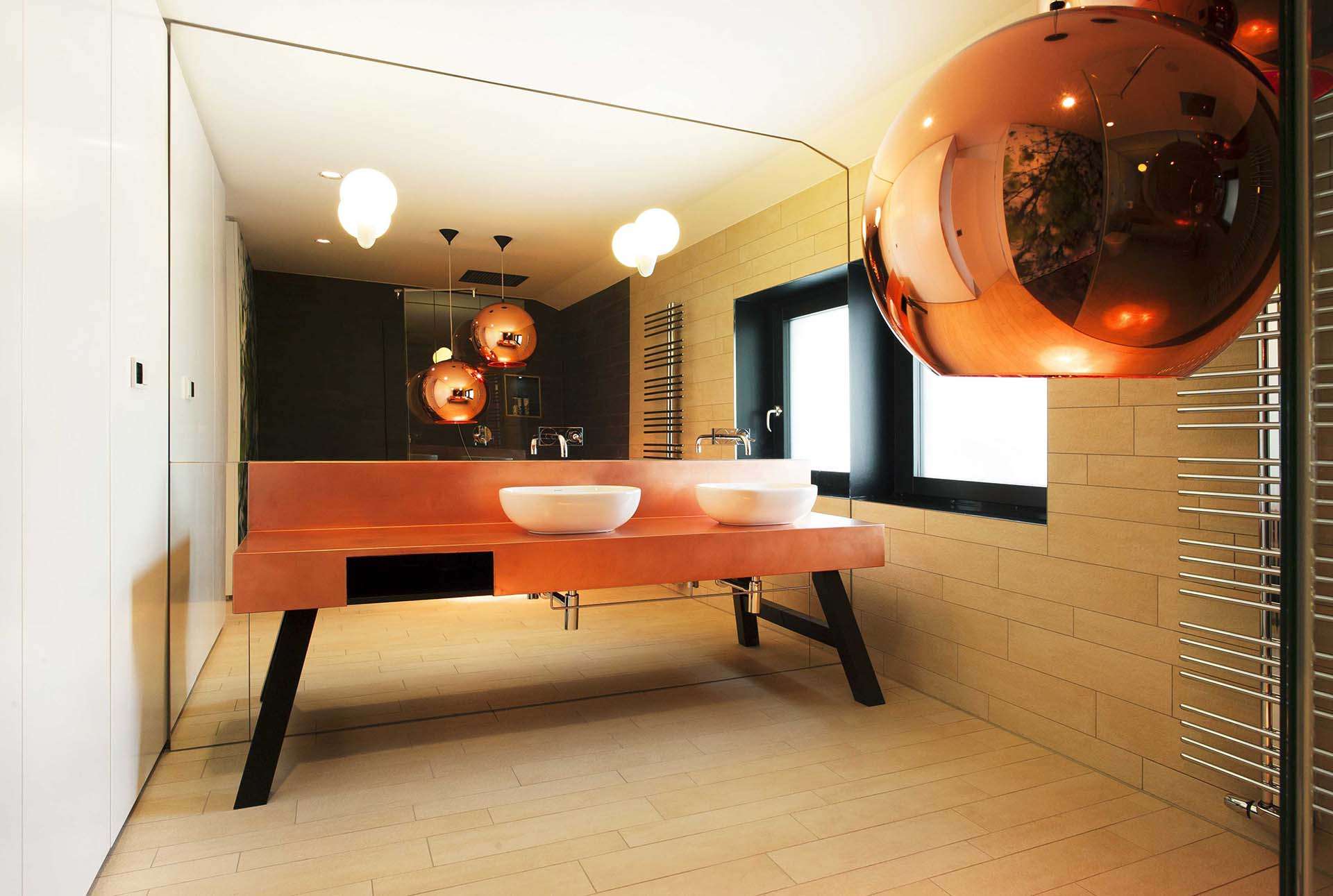 Rückwand des Waschtischs komplett verspiegelt. Freistehendes Badezimmermöbel in orange mit schwarzen Füßen. Runde Waschbecken aufliegend.