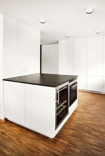 Quadratischer Küchenblock/Kücheninsel. Weiß mit schwarzer Stein-Arbeitsfläche. Küchengeräte integriert.