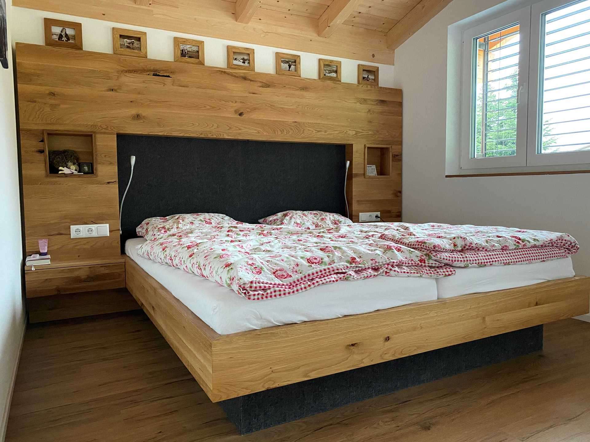 Holzverkleidete Rückwand und Massivholz-Bett mit schwarzem Kopfteil in Ferienwohnung in Immenstadt am Alpsee.
