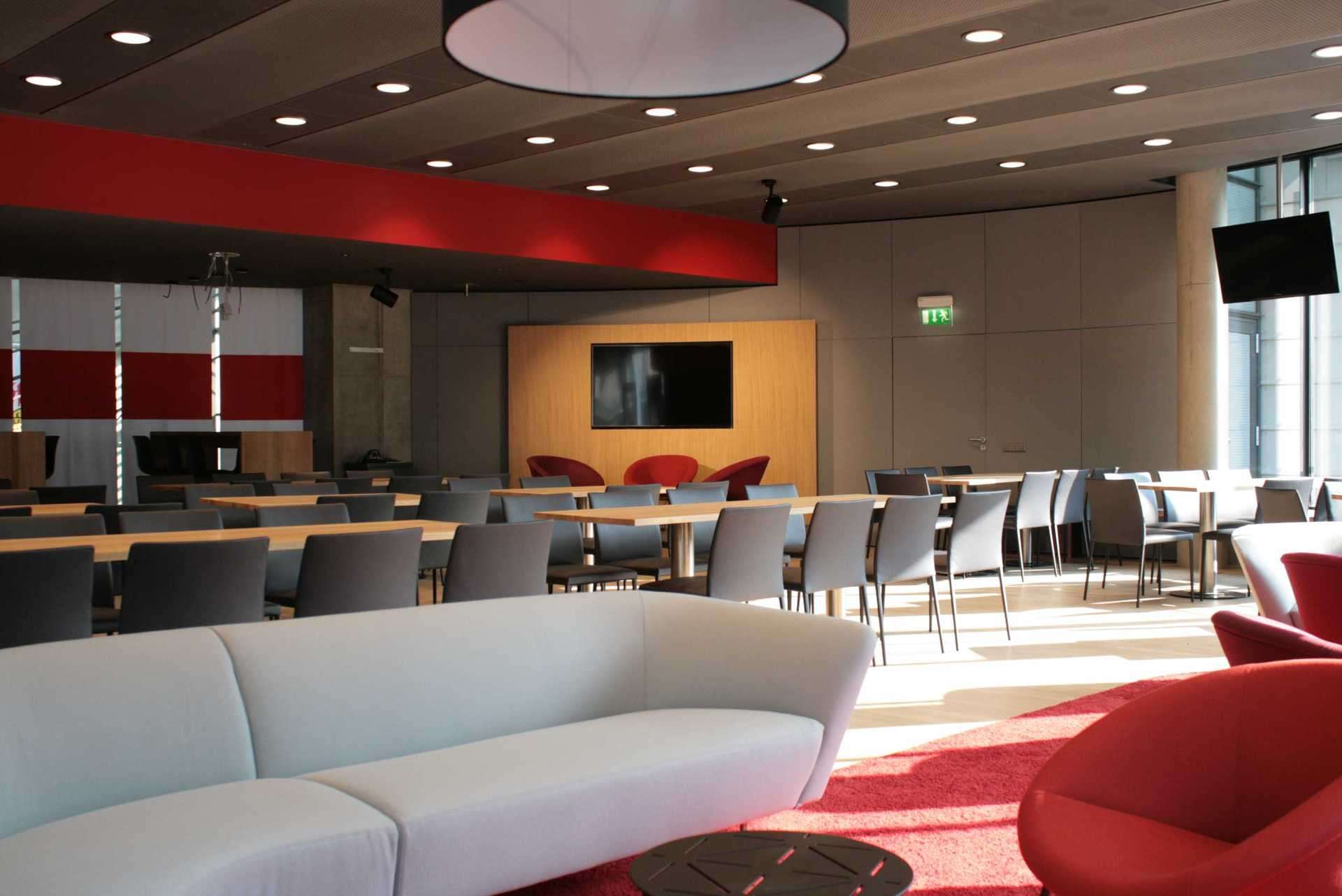 Lounge Ecke im Businessbereich Mercedes-Benz Arena Stuttgart, Sofas und Sessel in grau und rot. Runde Wandverkleidung in grau.