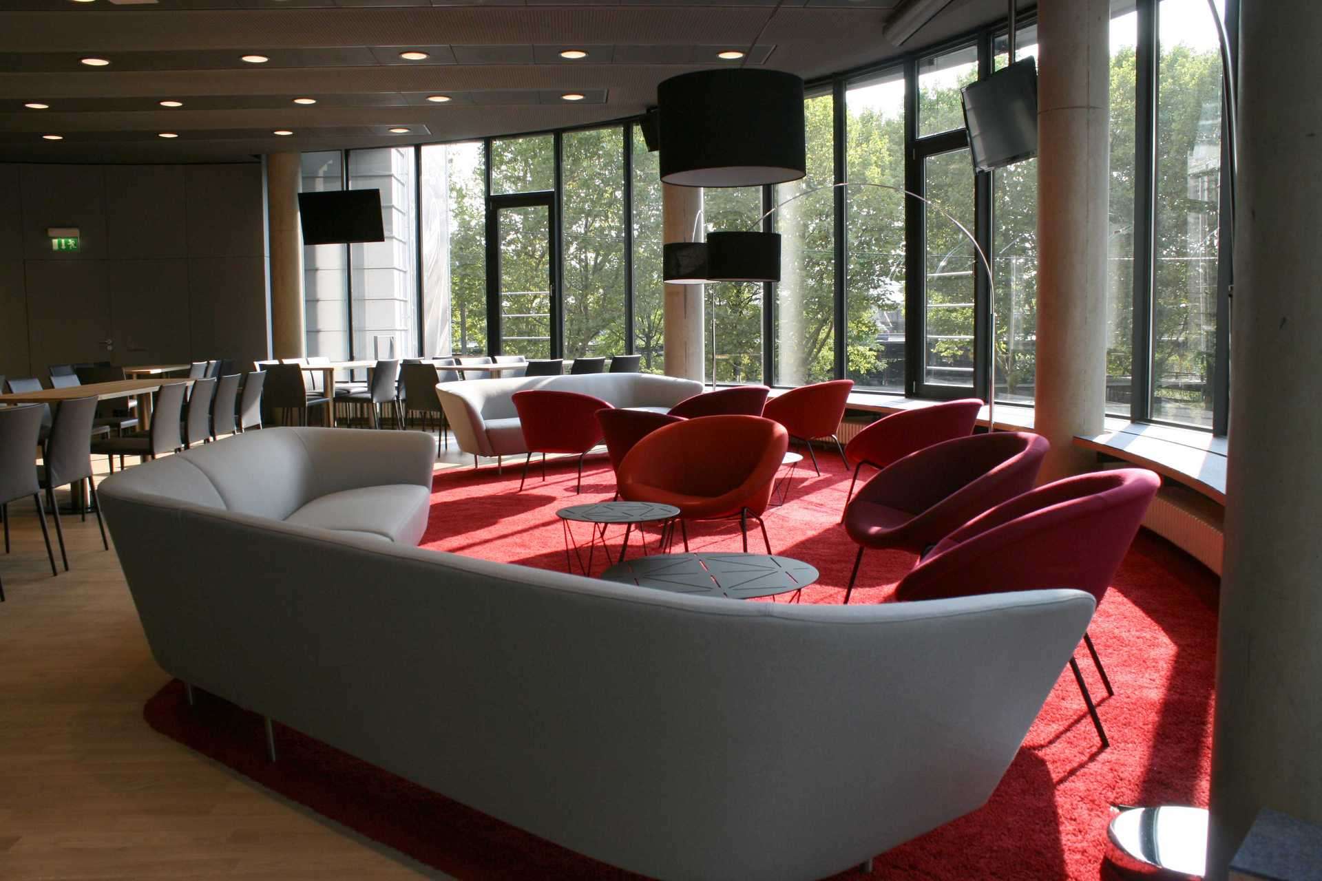 Lounge im Freundeskreis Raum des VfB Stuttgarts. Großes graues Sofa, roter Teppich und rote Sessel. Runde Verglasung nach außen.