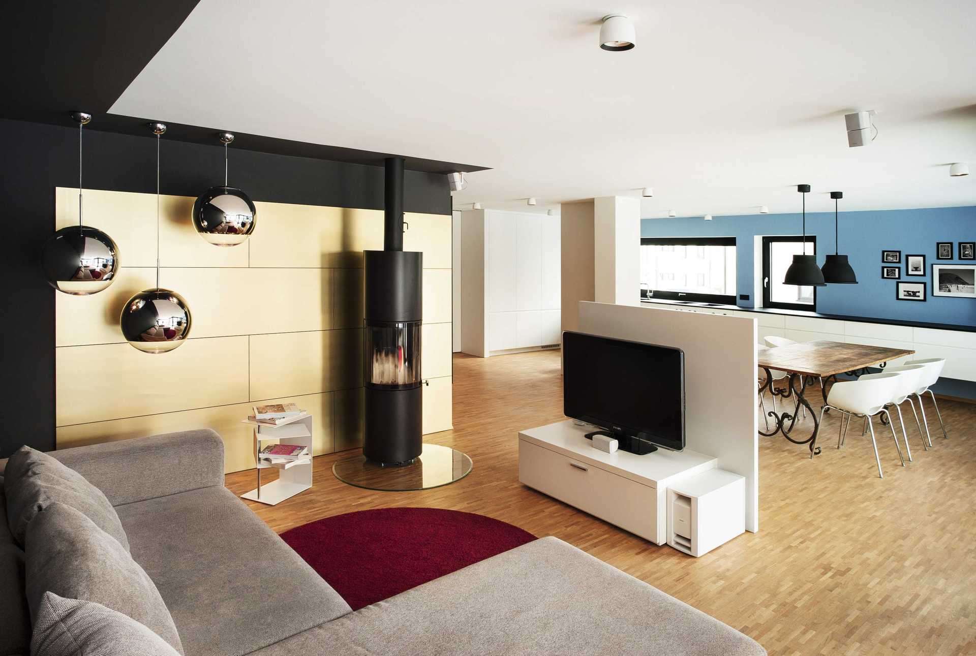 Goldene Wandverkleidung im Wohnzimmer als Rückwand des Kamins. Freistehendes Fernsehmöbel in der Mitte des Raums.