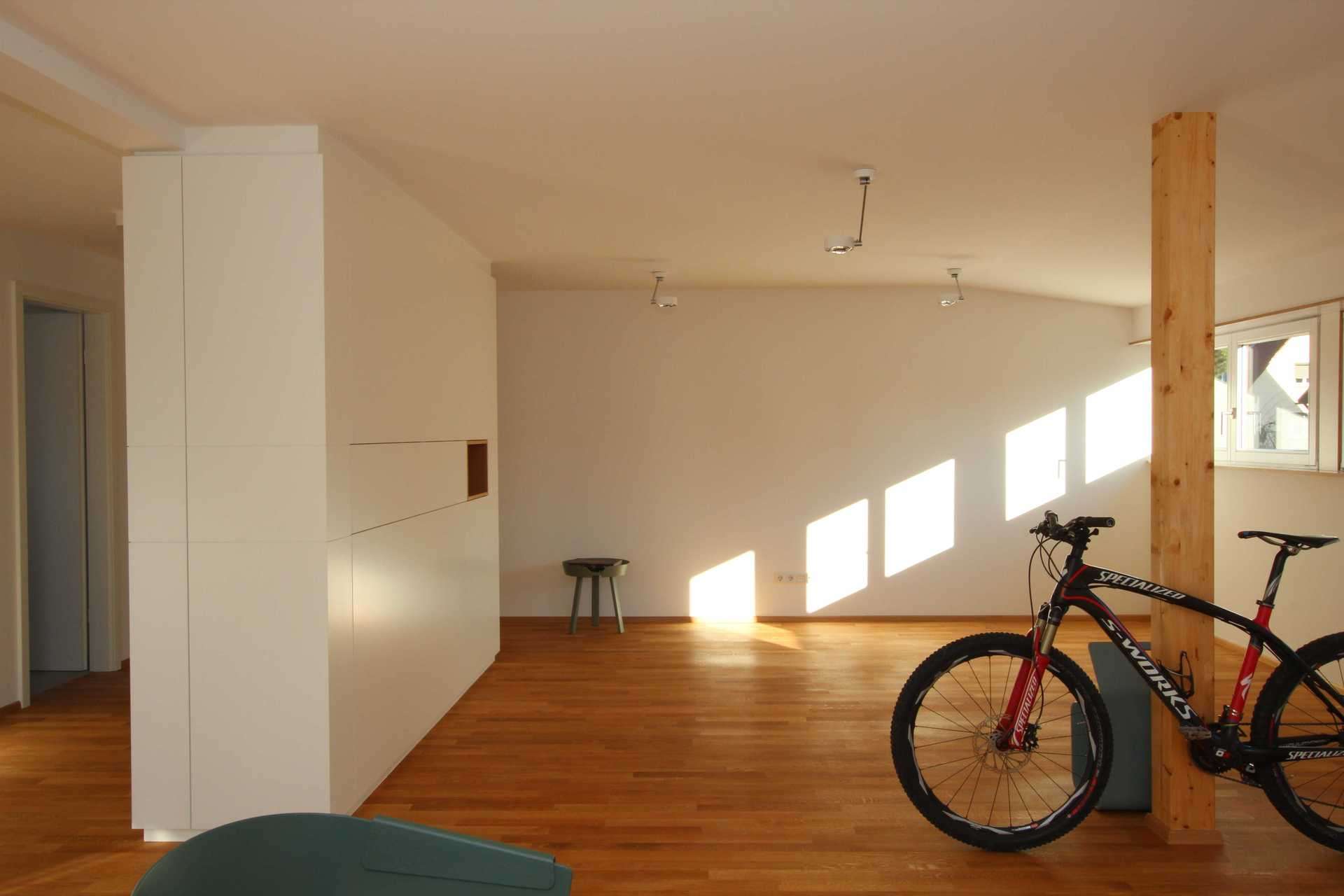 Freistehender Schrank als Raumtrenner, der den Eingangsbereich vom Wohnzimmer trennt. Komplett in weiß. Rennrad steht an Pfeiler im Raum.