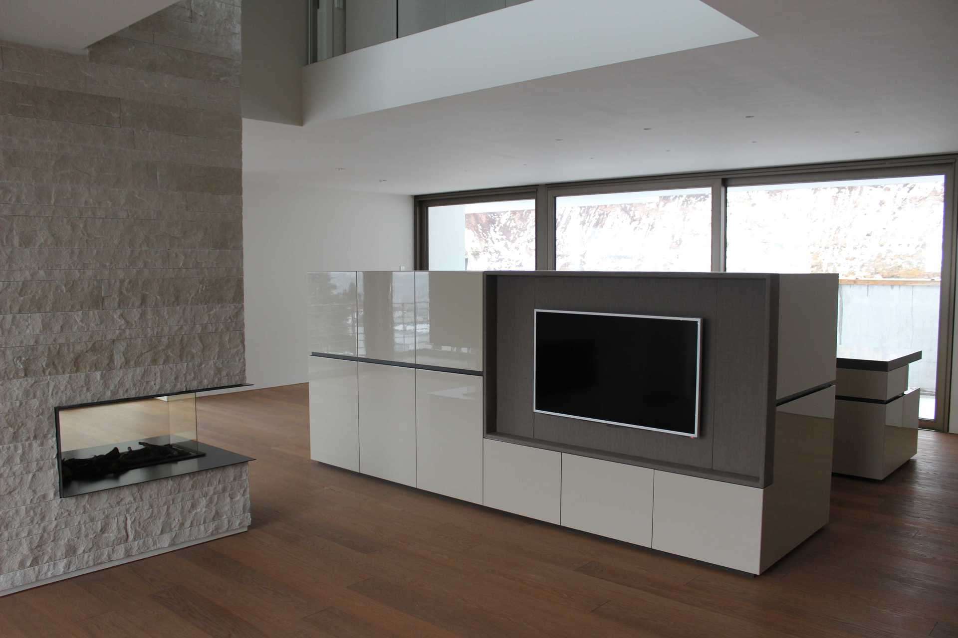 In die Rückwand der Küche ein Wohnzimmermöbel inklusiv Fernseher, freistehend im Raum. Weiß Glanz Lack, Rückwand hinter dem Fernseher in grau.
