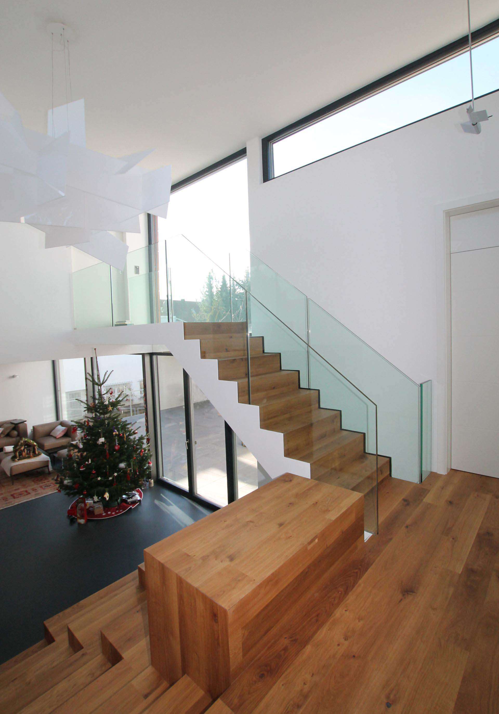 Breite Treppe aus Massivholz, Ansicht von oben, mit Sitzmöglichkeiten. Treppengelände aus Glas.